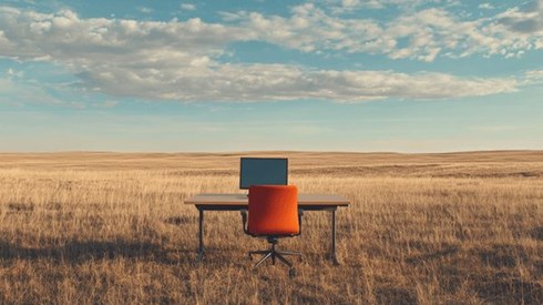 A desk with a computer monitor on it in the middle of the plains
