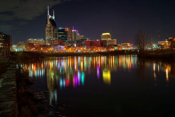 skyline of Nashville, Tennessee lit up with bright lights at night and reflected in the river