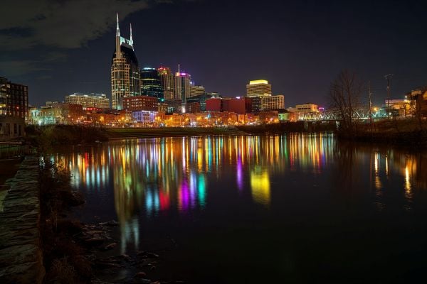 skyline of Nashville, Tennessee lit up with bright lights at night and reflected in the river