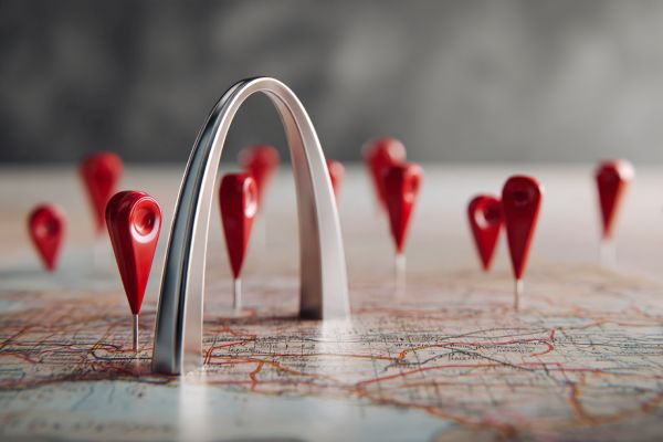 miniature pewter St Louis Arch and red map markers sitting on a US map