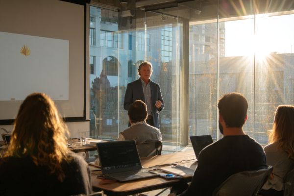 instructor talking to adult business professional students in a classroom in front of a window with the sun glinting through it