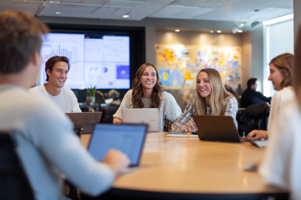 students happily chatting around a conference table with laptops in front of them