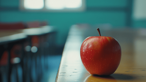 A red apple sitting on the corner of a teacher's desk
