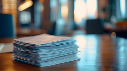 A tidy stack of papers rests on a wooden desk.