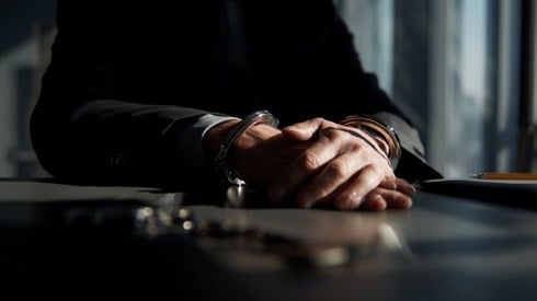 handcuffs around the wrists of a businessman in a darkened conference room