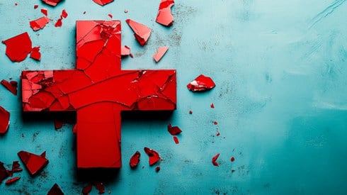 A red medical cross with several cracks on its surface, and broken fragments resting around it.