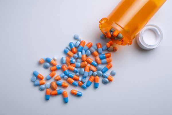 blue and orange pills and capsules coming out of a generic prescription bottle lying on a white background