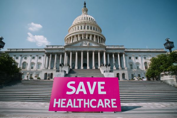 a pink "Save Healthcare" sign in front of the US Capitol building