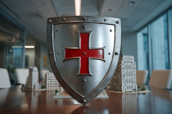 silver knight's shield with a red cross in front of a model commercial business building on a conference table