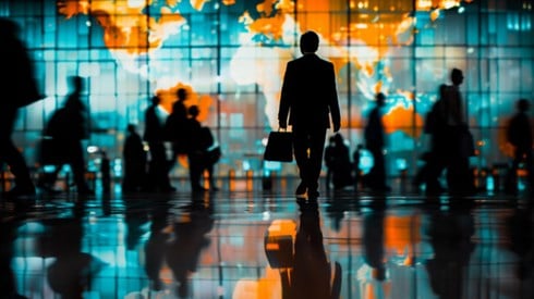 Silhouettes of business professionals walking around a large room, with a glowing world map in the background.
