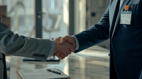 a businessman shakes hands with a man wearing a visitor's name tag in an office boardroom