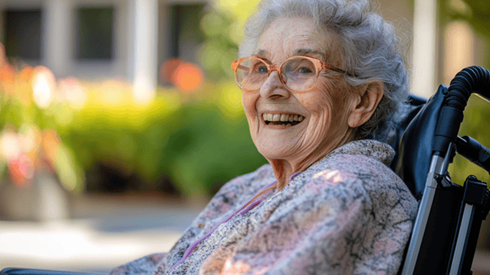 An elderly woman smiles while outside in a wheelchair