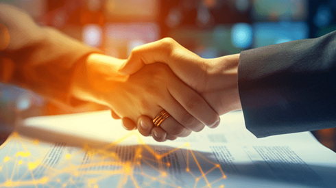 A closeup of a handshake between two people with paperwork beneath the handshake
