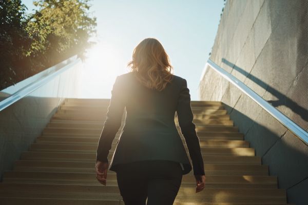 the back of a businesswoman walking up stairs into the sun