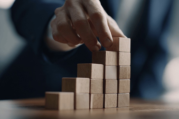 A close-up of the hand of a businesswoman building a structure with wooden blocks