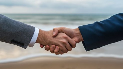 two businesspeople's hands shaking on a beach
