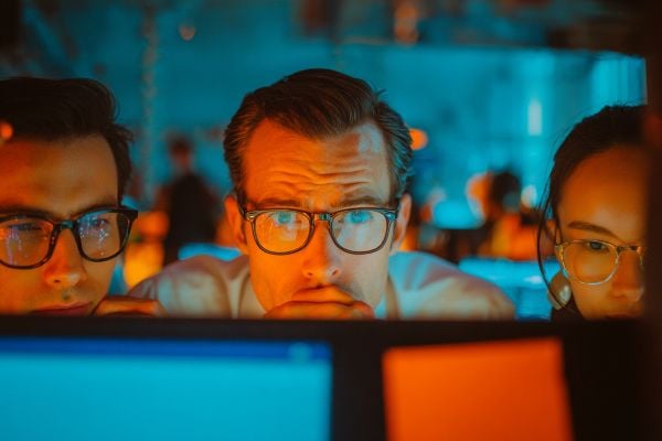 three business professionals looking at computer screens lit with blue and orange lights