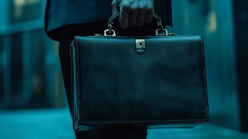 Closeup of a black leather briefcase being carried by a businessman in a dark blue suit