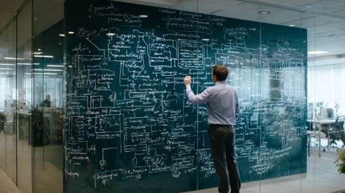 businessman drawing a confusing flowchart on a glass wall in a professional office