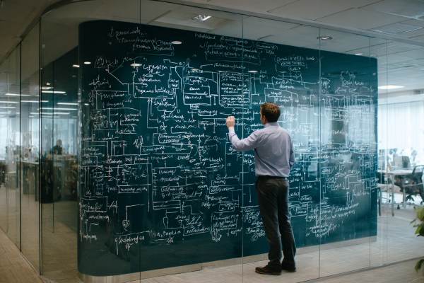 businessman drawing a confusing flowchart on a glass wall in a professional office