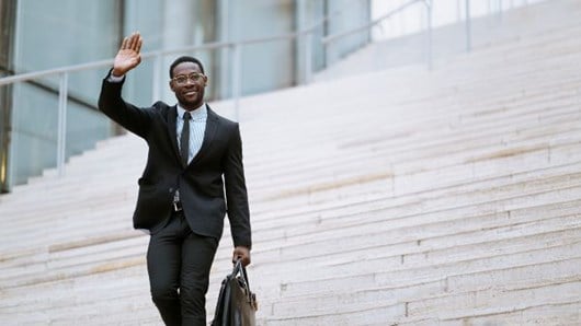 businessman carrying a briefcase walking down outdoor stairs waving