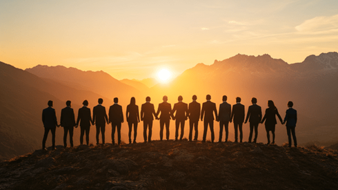 A group of businesspeople standing in a line holding hands on the ridge of a mountain as the sun rises behind the mountains