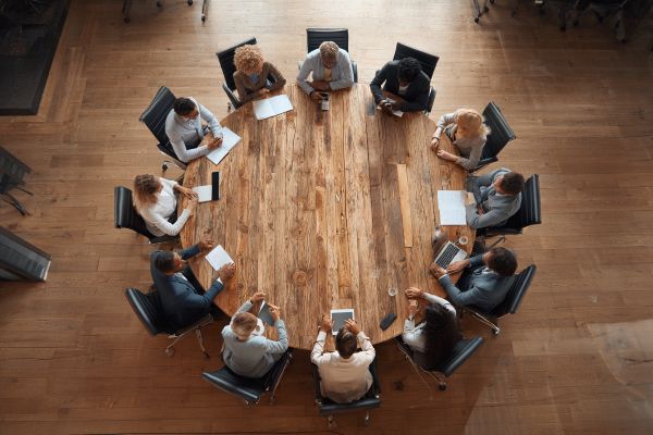 overhead view of younger businesspeople sitting around a wooden round conference table