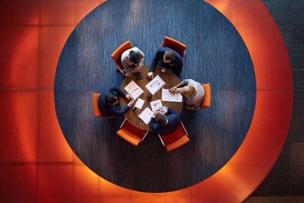 Overhead view of businesspeople meeting around a round wooden table on dark blue carpet and a glowing red floor
