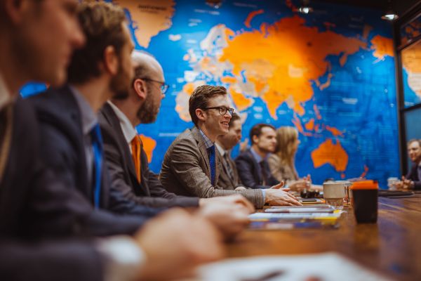businesspeople sitting at a table with an orange and blue world map behind them