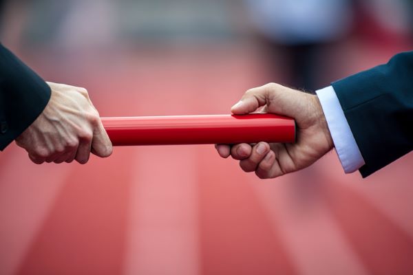 businessperson passing a baton to a second person over a race track