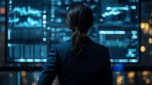 A businesswoman in a dark blue suit in front of a high-tech screen with various graphs and charts on it