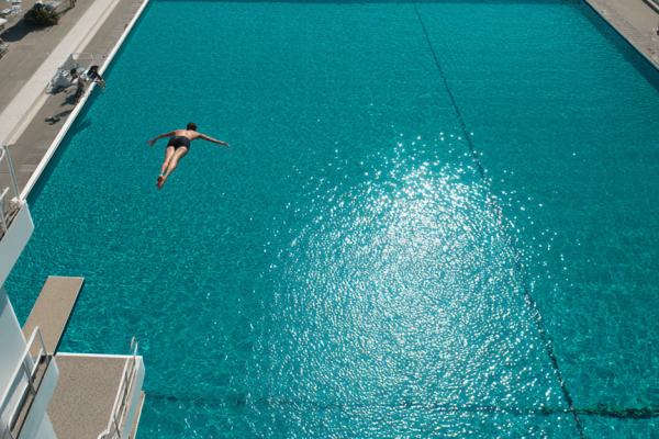 A diver in midair above a large swimming pool