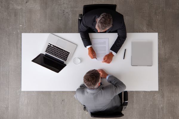 overhead view of two businesspeople talking over a white desk and a laptop