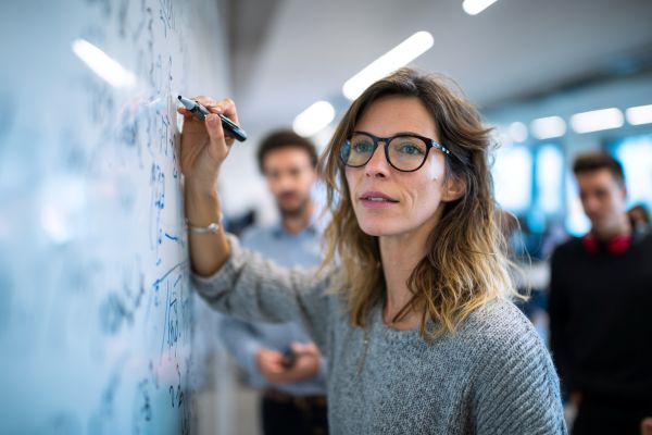 professor writing on a white board in front of students
