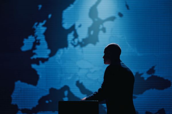 silhouette of a businessman standing at a podium in front of a blue map of Europe on the wall