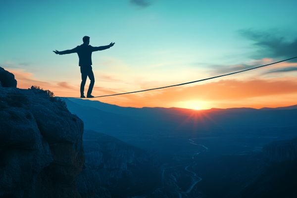 silhouette of a businessman balancing on a tightrope walking over a valley at sunrise