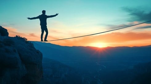 silhouette of a businessman balancing on a tightrope walking over a valley at sunrise