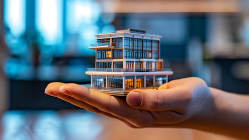 A miniature office building resting in the palm of a hand.