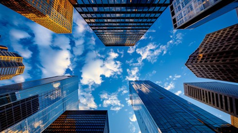 A collection of skyscrapers reaching towards the clouds in a blue sky, seen from street level looking upwards.