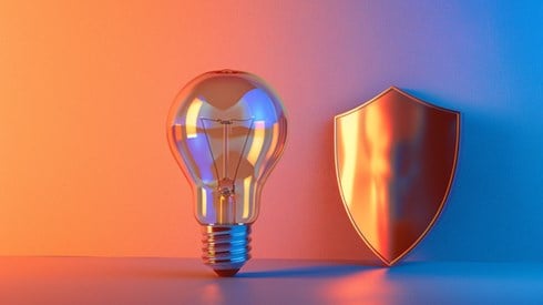 A light bulb standing next to a sleek shield, with a bright orange and blue gradient background.