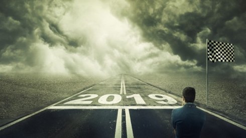 A businessman contemplates a racetrack with a starting line and flag at 2019 and the road ahead is dark with thick clouds