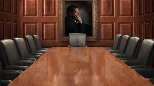Empty board room table with black executive chairs and portrait of a man on wood paneled walls