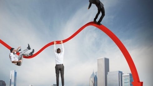 City skyline with curving, downward red arrow in the sky, and three businessmen trying not to fall off the arrow