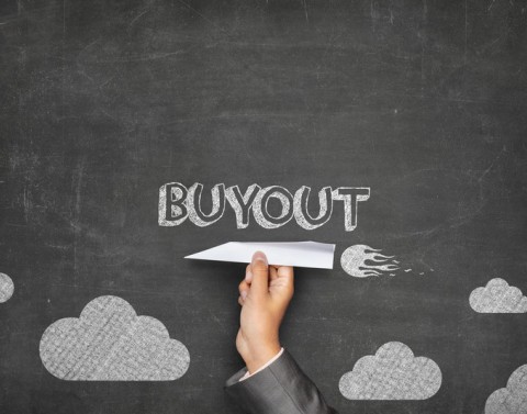 A businessman holds a paper plane in front of a blackboard that has drawings of clouds and the word BUYOUT