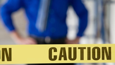 Yellow tape with the word CAUTION in black print and a man standing in the background white his hands on his hips