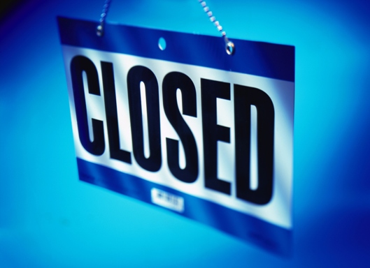 A CLOSED sign hanging from a chain with black letters on white and blue stripe above and below letters