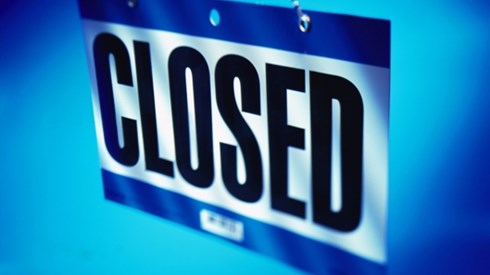 A CLOSED sign hanging from a chain with black letters on white and blue stripe above and below letters