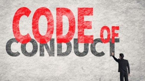 A full-sized businessman standing and pointing to the giant phrase CODE OF CONDUCT