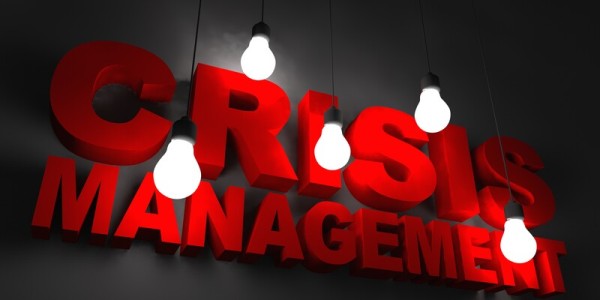 Crisis Management in Red Letters Illuminated by Hanging Lightbulbs