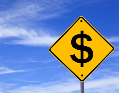 Yellow diamond-shaped traffic warning sign showing a dollar sign with a blue sky background.